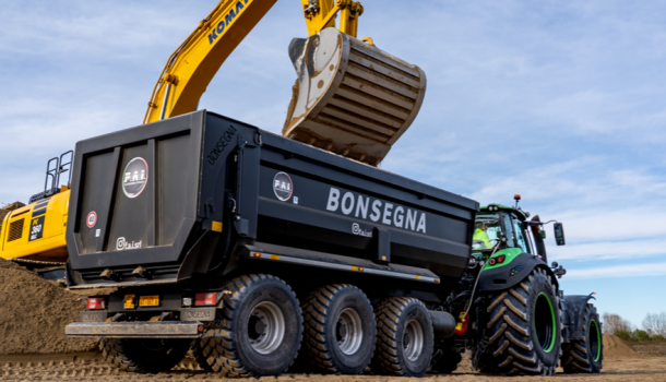 Escavatore giallo che carica terra su un dumper Bonsegna trainato da trattore su un cantiere